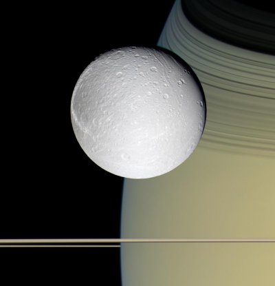 Dione vista con Saturno y sus delgados anillos. Crédito: Cassini/NASA.