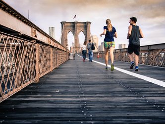 Two people running over a city bridge