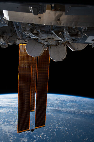 The International Space Station's main solar arrays drape across the Earth above the Pacific Ocean west of Hawaii.