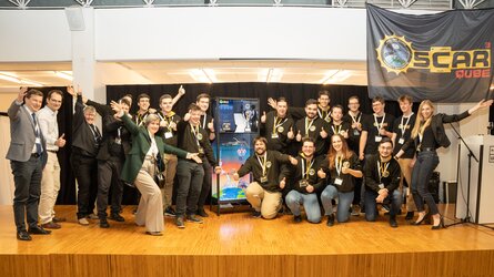 The OSCAR QUBE team, the sponsors and the experiment in its display case. 