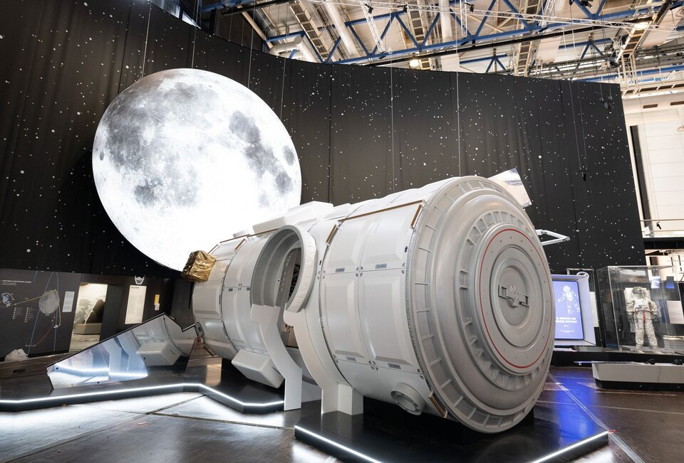 A 7-meter-diameter Moon watches over the full-scale model of the I-Hab module of the future Gateway lunar station