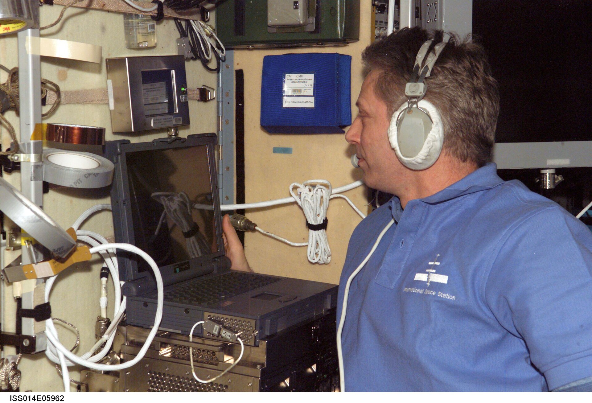 Thomas Reiter wears a communication system headset while using a computer in the Zvezda