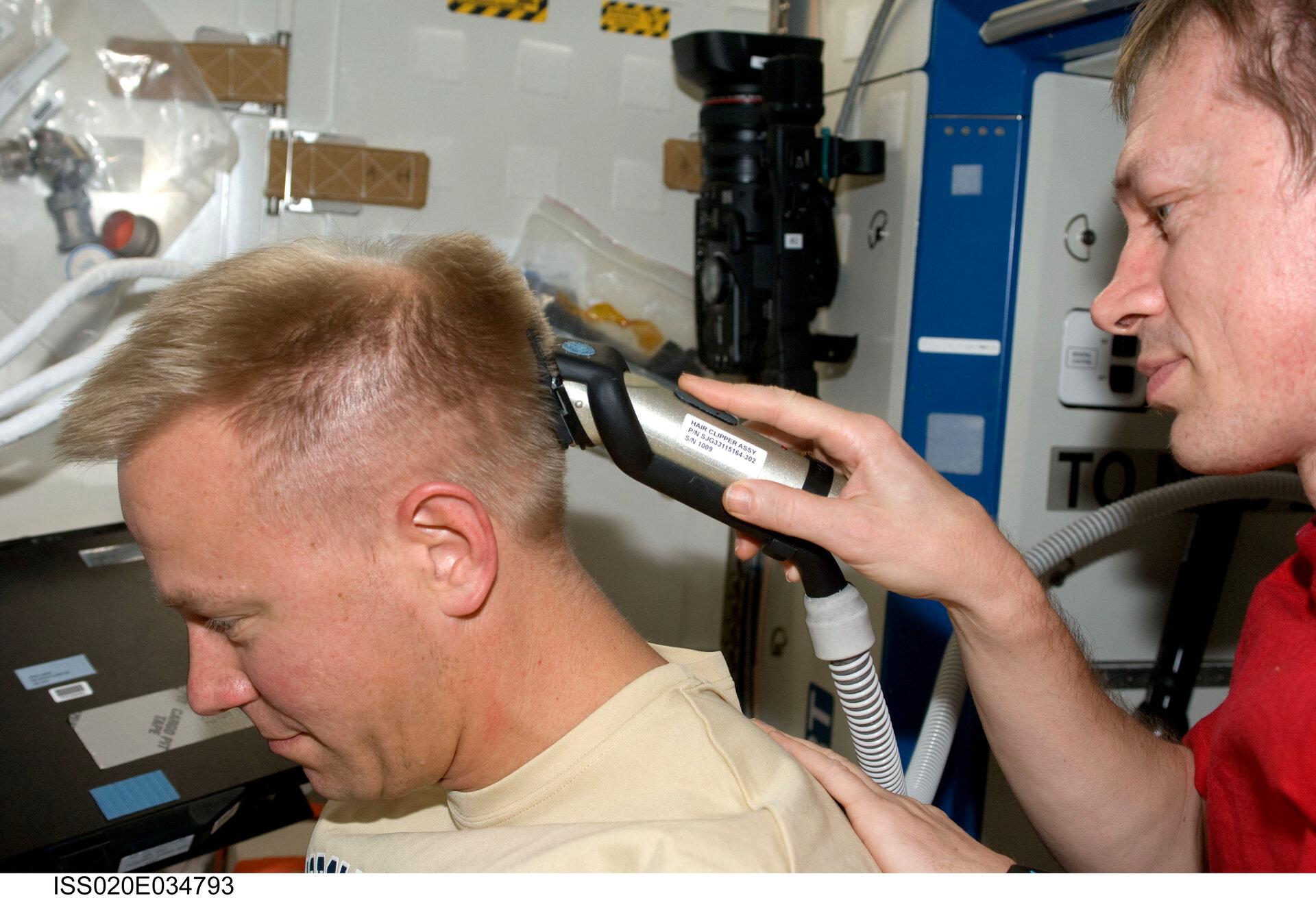 Frank De Winne cuts Tim Kopra's hair using hair clippers fashioned with a vacuum device