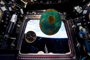 Nebra Sky Disc floating next to Matthias Maurer's Cosmic Kiss mission patch in Cupola