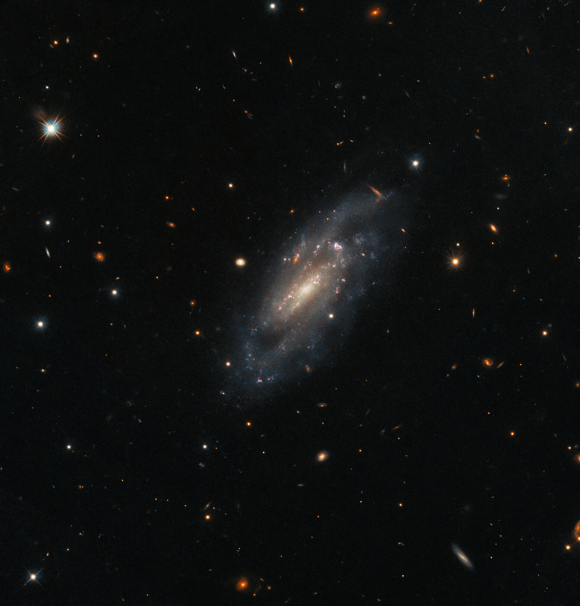 La galaxia es central en un campo de pequeñas estrellas y galaxias sobre un fondo oscuro. Crédito: ESA / Hubble & NASA, A. Filippenko, J. D. Lyman