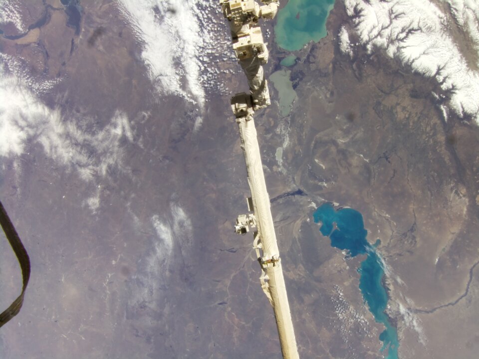 A photo taken by the Astro Pis of the Earth’s surface with a robotic arm in view.  