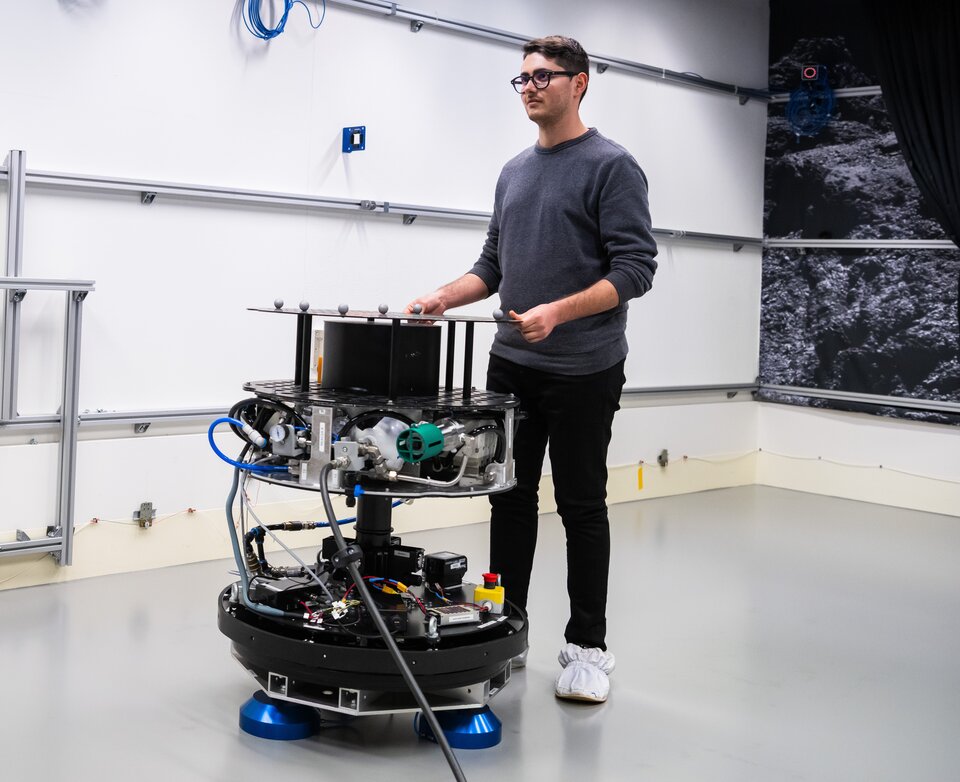 A member of the GRASP team manoeuvring a floating platform on the flat floor of the Orbital Robotics Lab